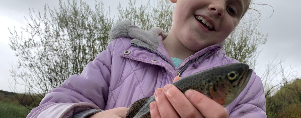Little girl holding a rainbow trout and smiling