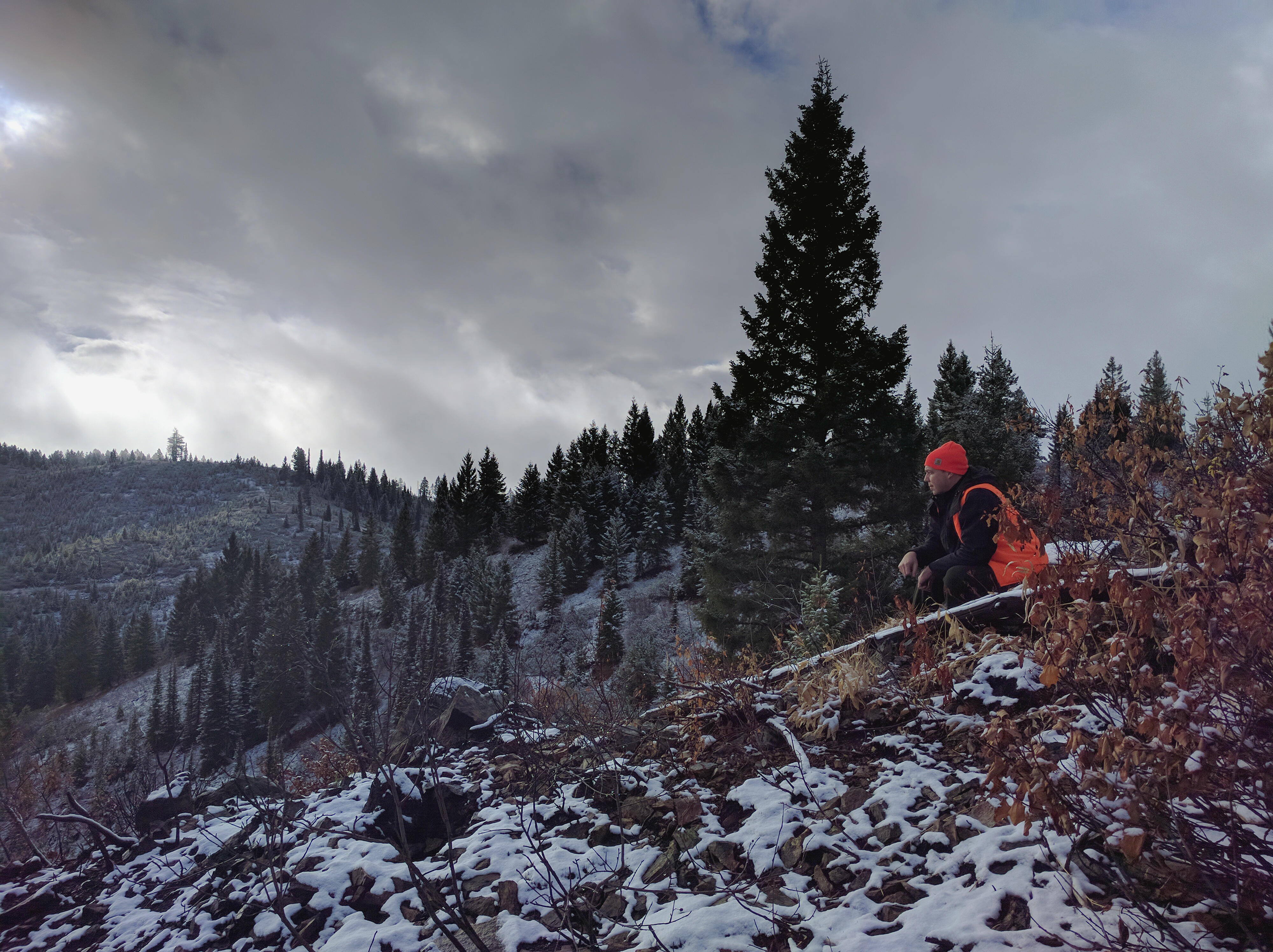big game hunter dressed in hunter orange looking for game on a mountain ridge with some snow on the ground Ben Studer medium shot, November 2016