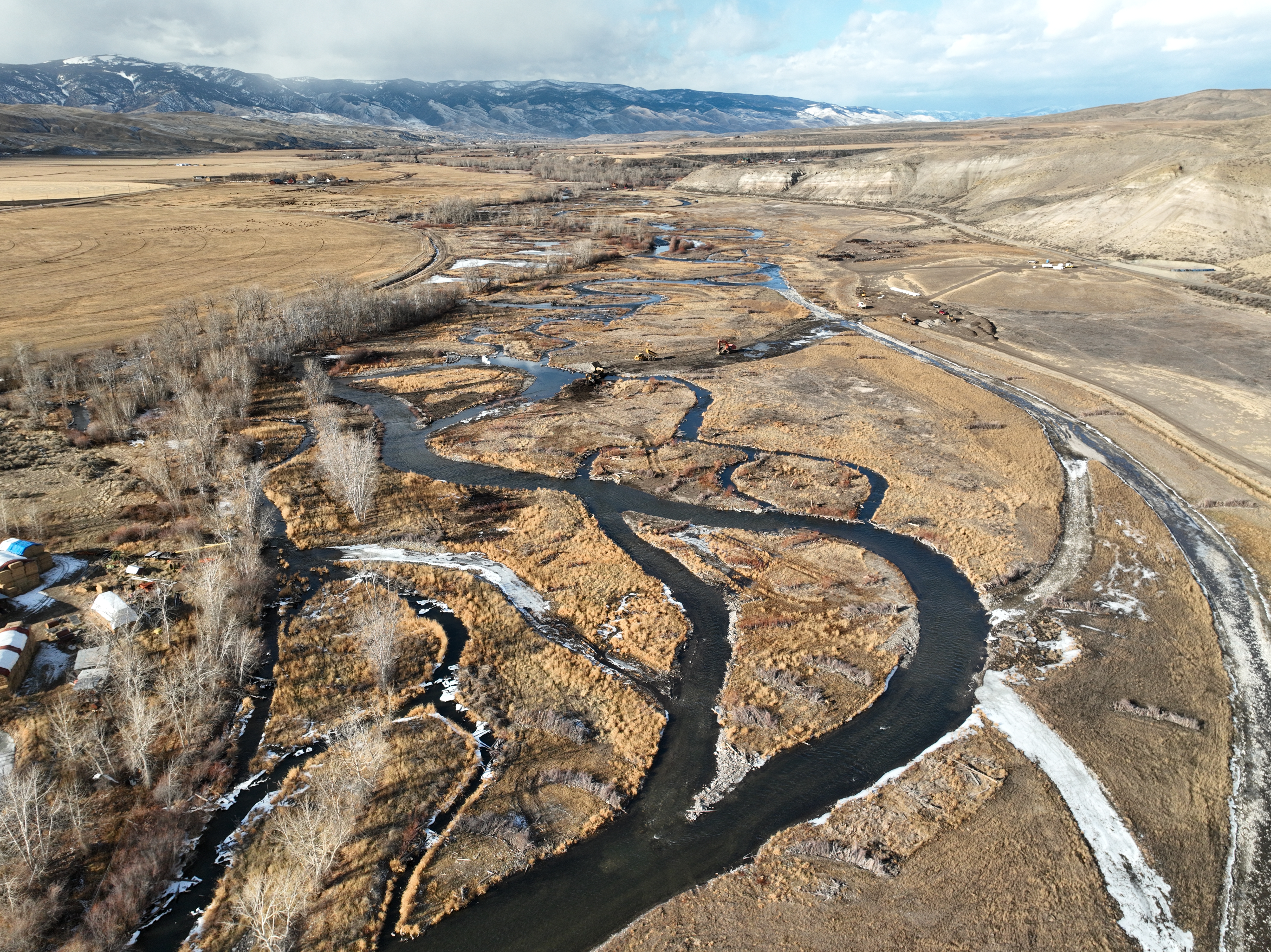 A windy river that splits many times takes up most of the width of an agricultural field
