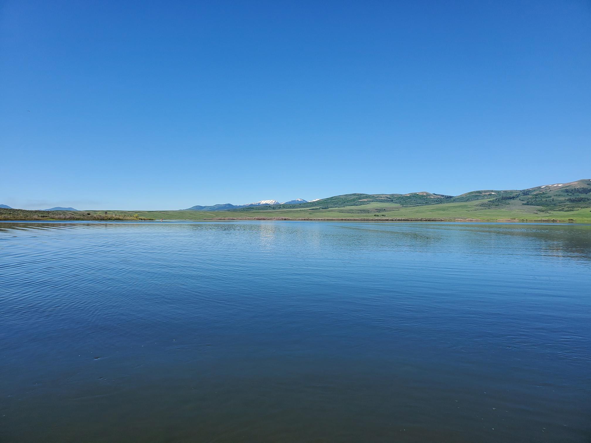 large blue still reservoir with matching blue sky and vegetation-covered land in the distance