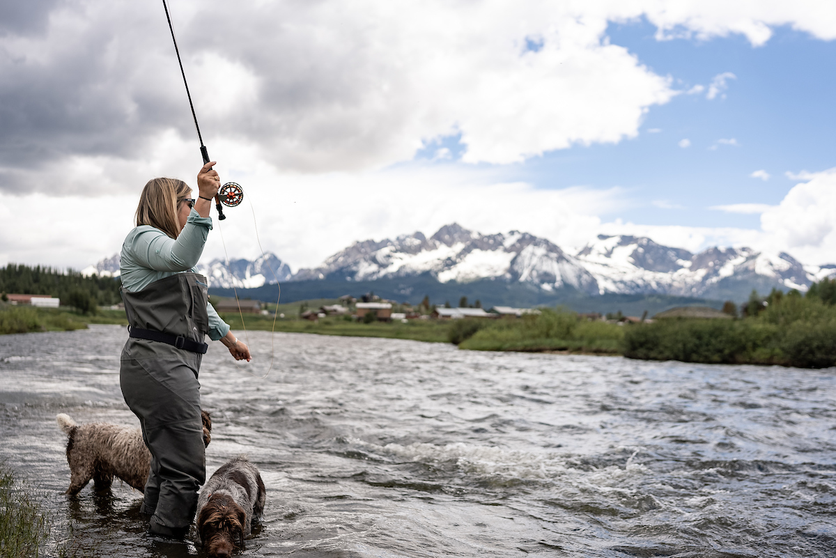 With her two dogs standing next to her, an angler fly fishes in the Salmon River near Stanley.