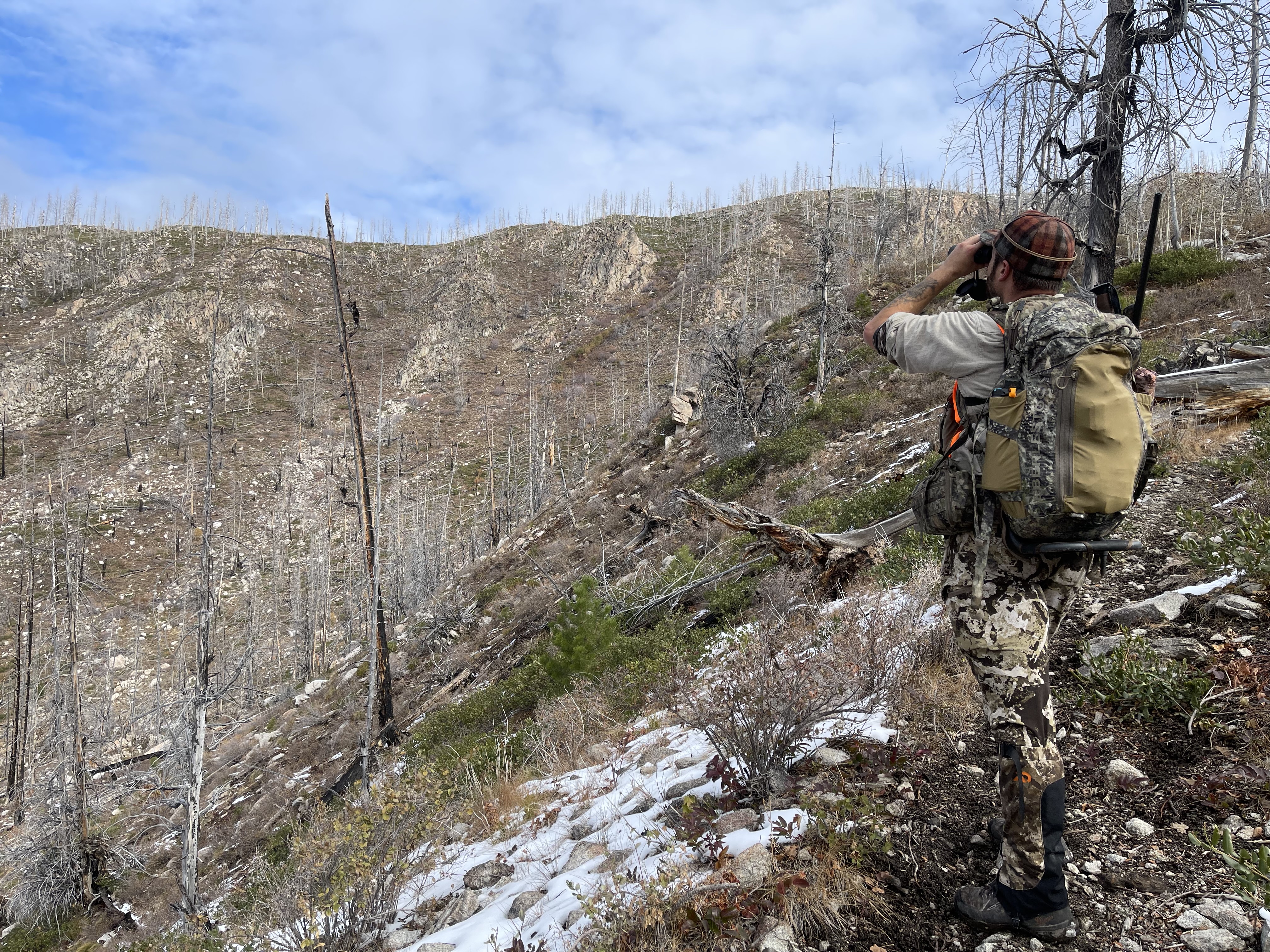 Hunter glassing a hillside in late fall snow