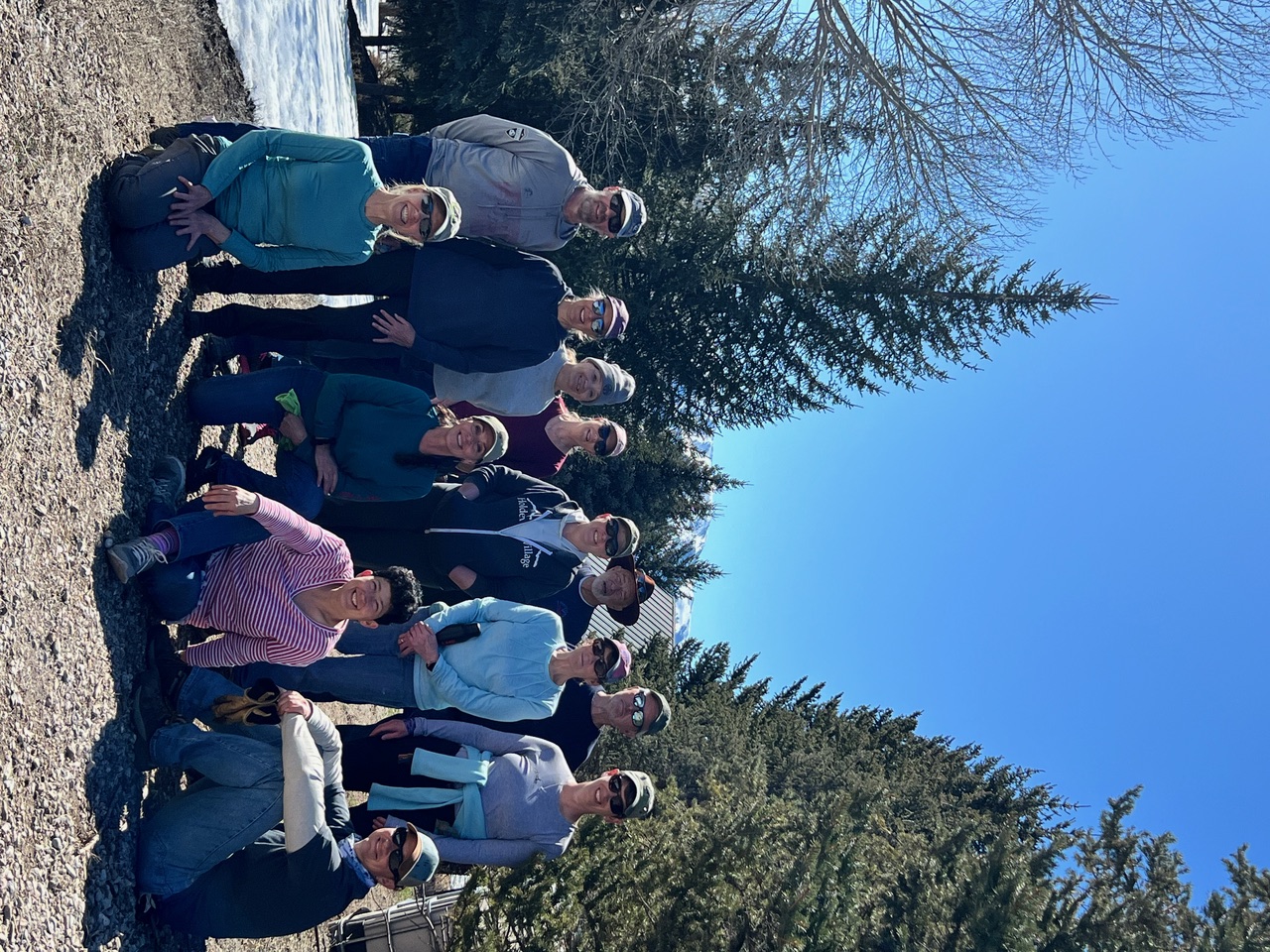 Group of people standing side by side outside with green trees in the background. 