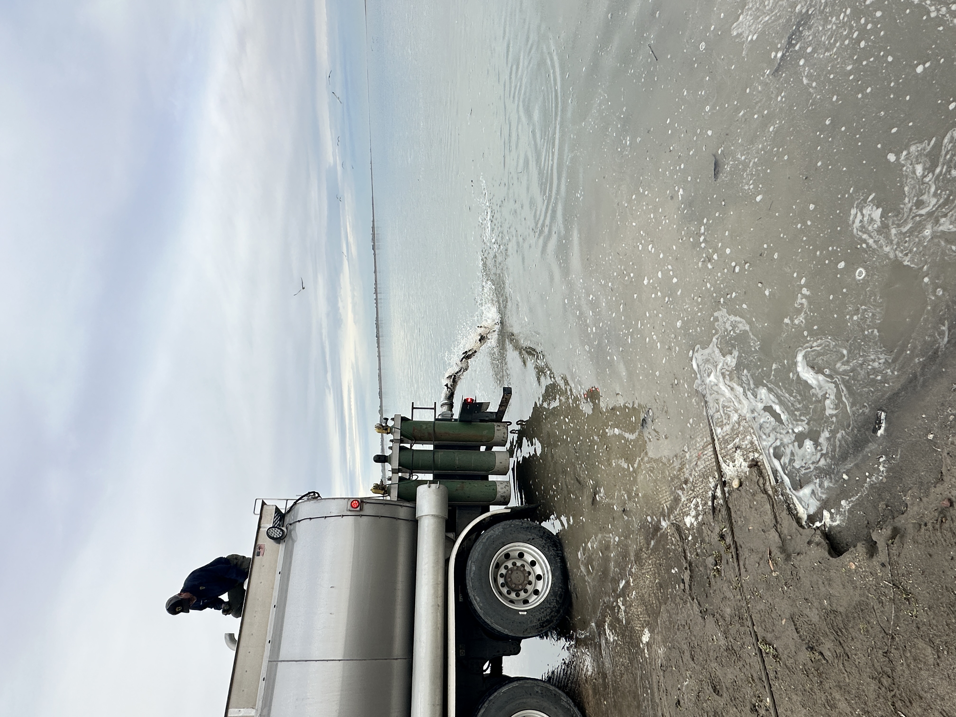 Large silver truck releasing fish to large body of water.