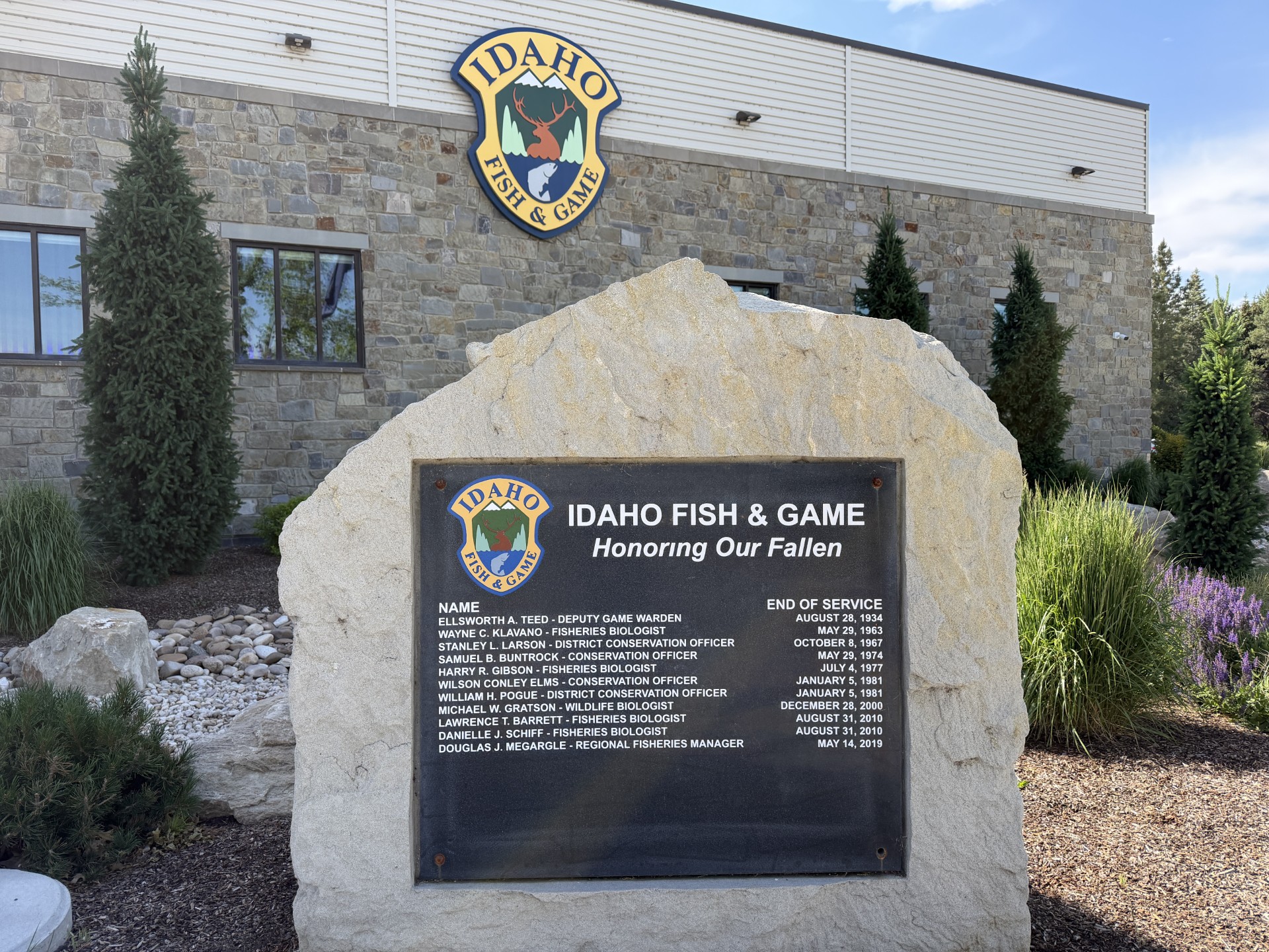 Light colored rock with memorial plaque noting fallen IDFG employees with IDFG headquarters building in the background