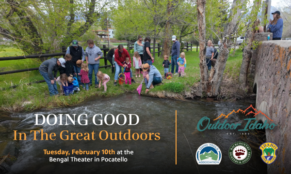 Group of people of all ages standing on green grass in front of a brown fence.   They are part of an outdoor volunteer project.