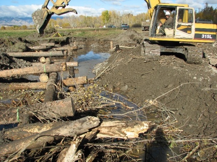 An excavator builds large log structures in a newly constructed river bend