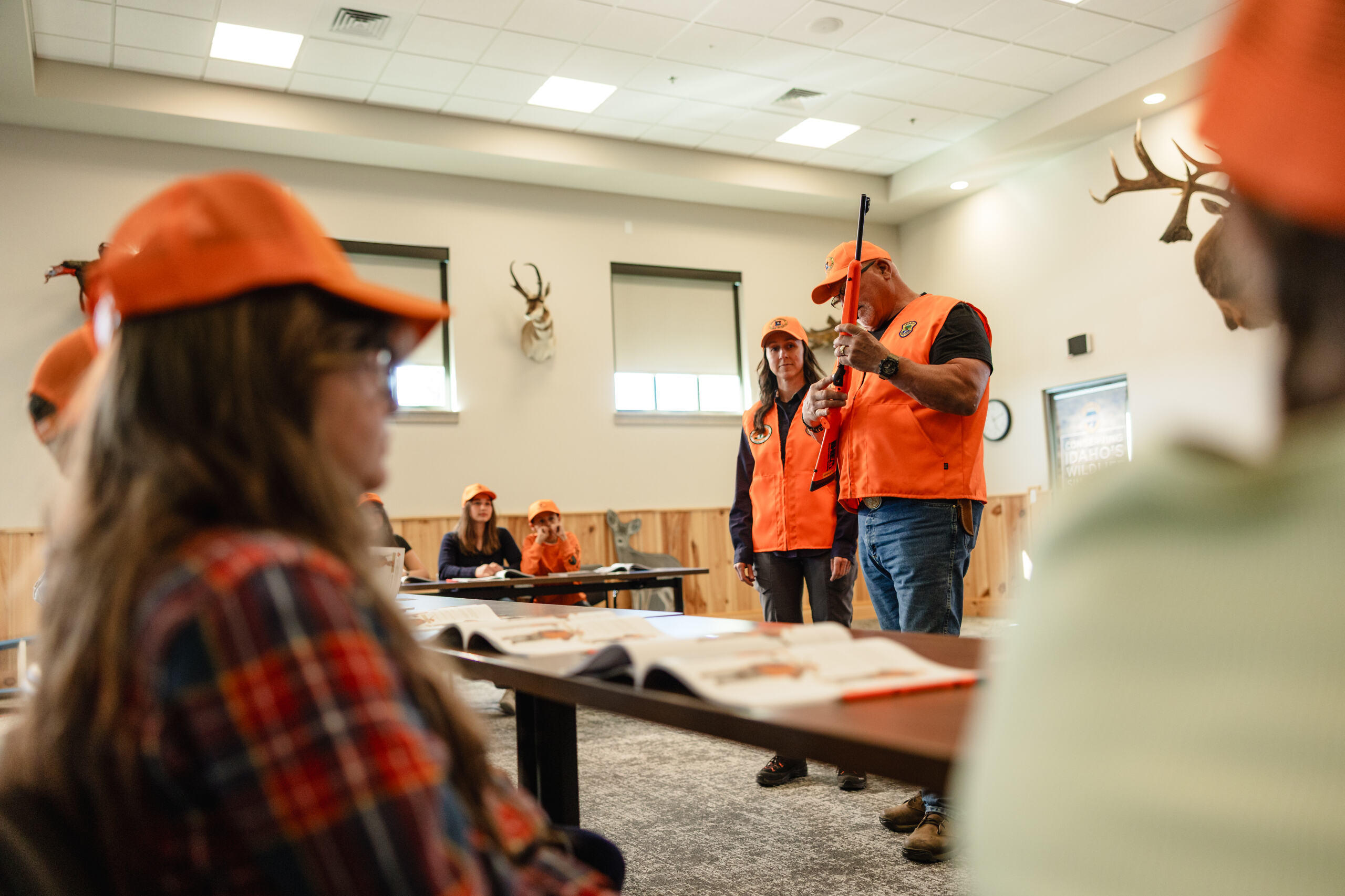 A hunter education instructor holding a firearm points at the trigger in front of a class.