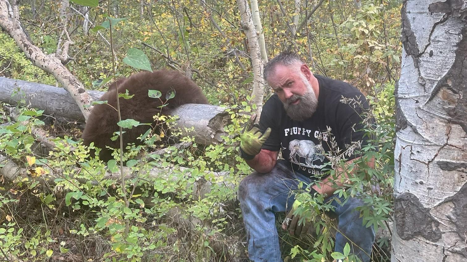 Joelseph Jenkins sitting on a log in the forest next to an illegally harvested black bear 