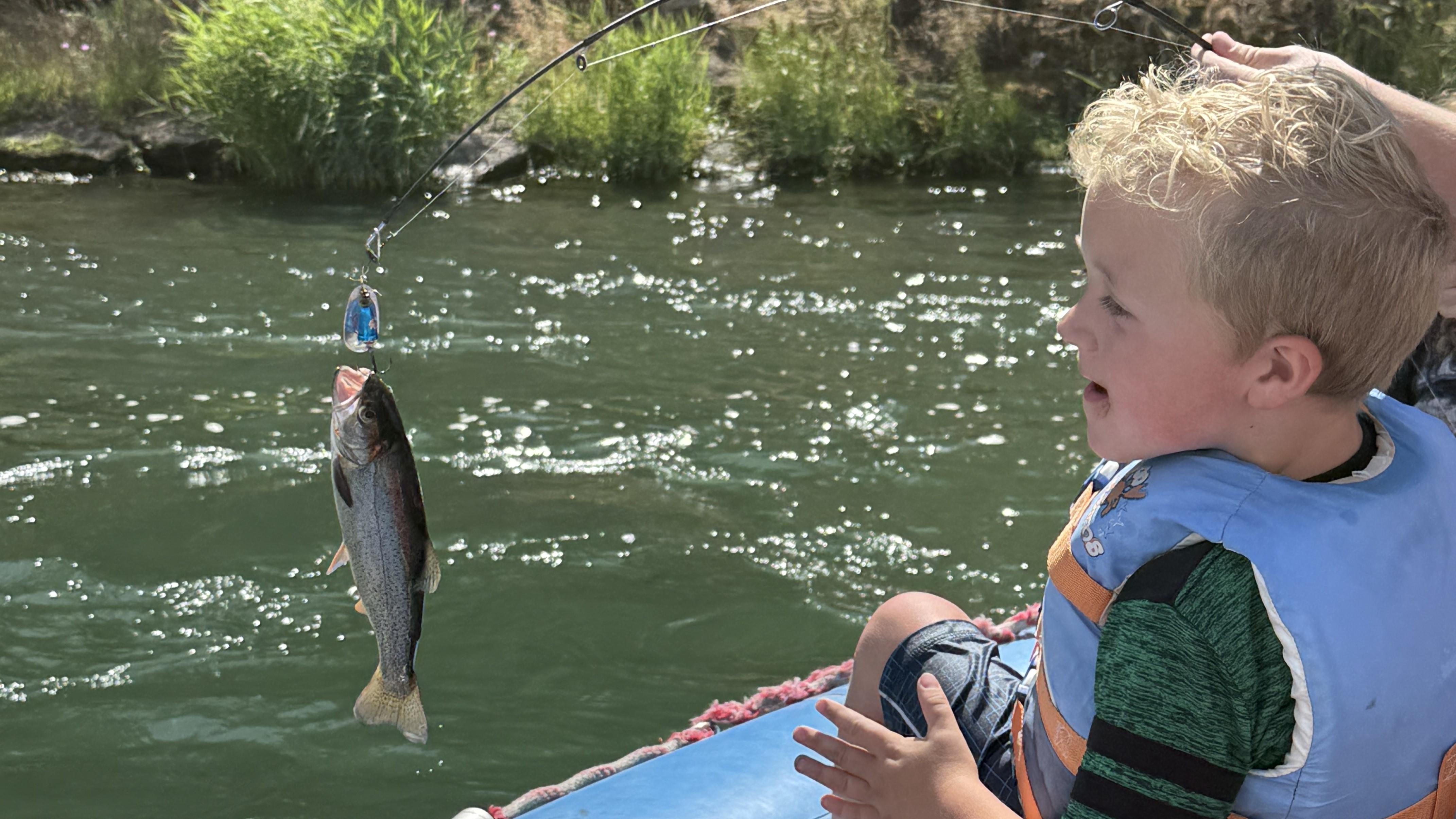 Kid on a raft smiling at a fish that was just caught.