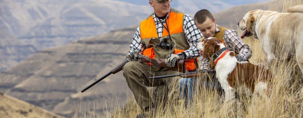 medium shot of a man and boy with their dogs dressed in hunter orange taking a break from hunting October 2015