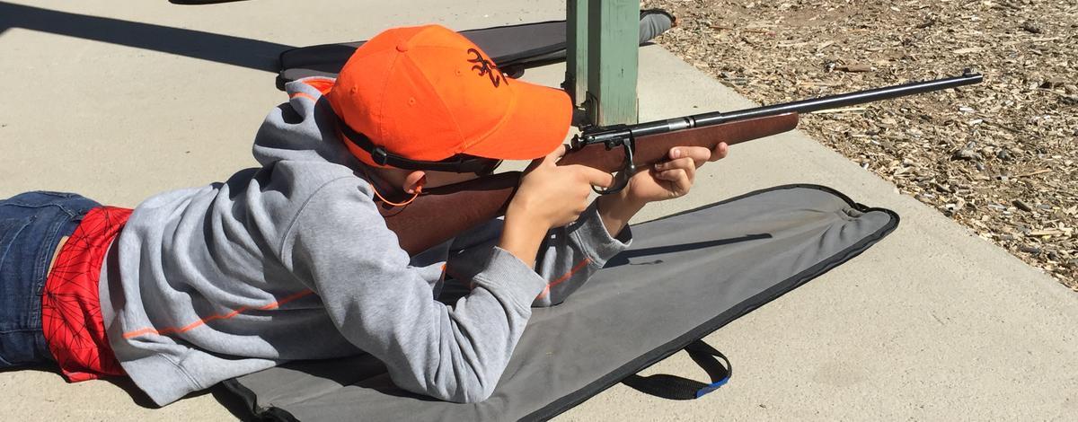 boy wearing a hunter orange cap learning how to fire a rifle during a Hunter Education class August 2016