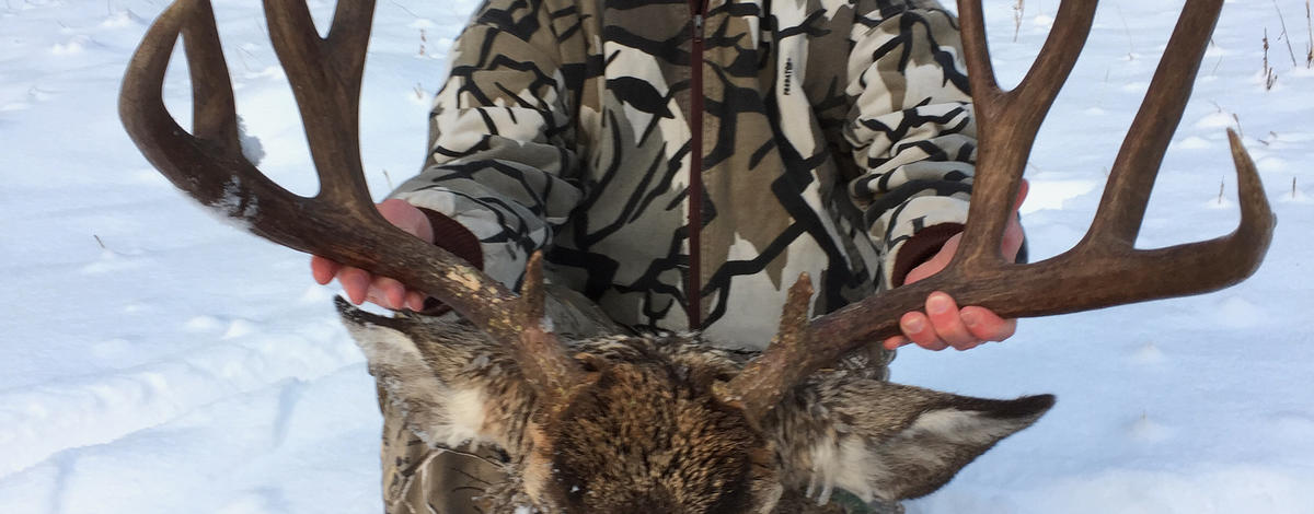 man with his big mule deer buck and rifle in snow vertical shot November 2016