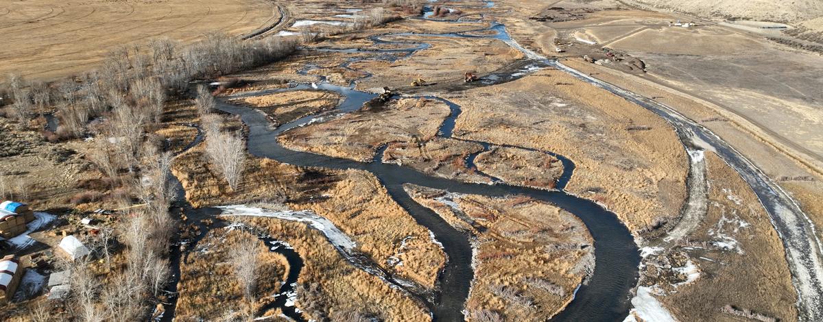 A windy river that splits many times takes up most of the width of an agricultural field