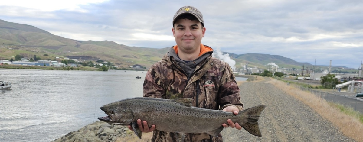 An angler stands along the Clearwater River with a Chinook salmon