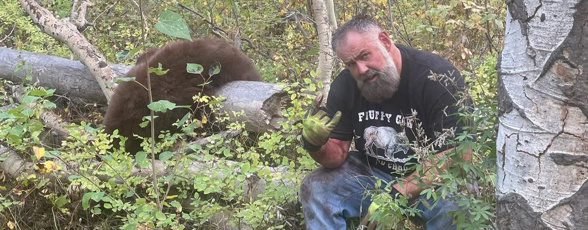 Joelseph Jenkins sitting on a log in the forest next to an illegally harvested black bear 