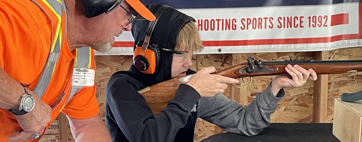 Hunter education instructor assisting student with live fire