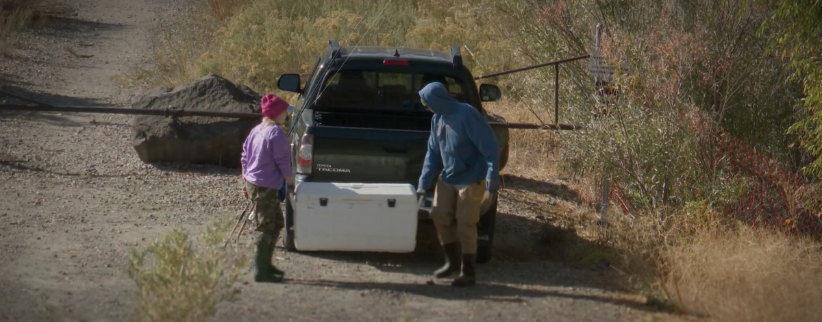 Two anglers carry a cooler to a pickup truck