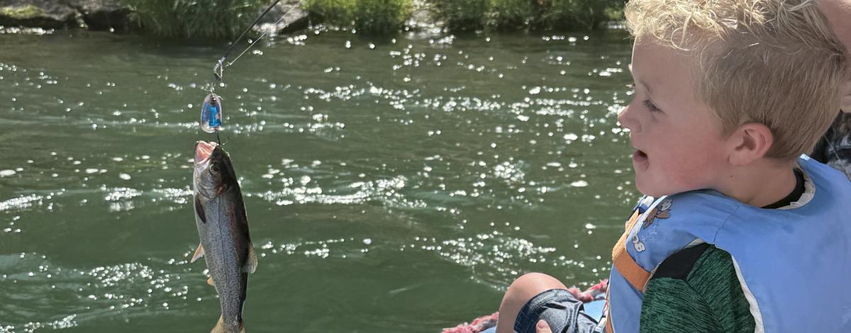Kid on a raft smiling at a fish that was just caught.