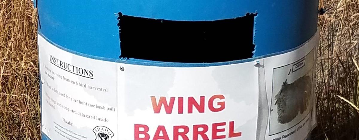  A blue barrel sits in a field of grass with the words "wing barrel" across it. 