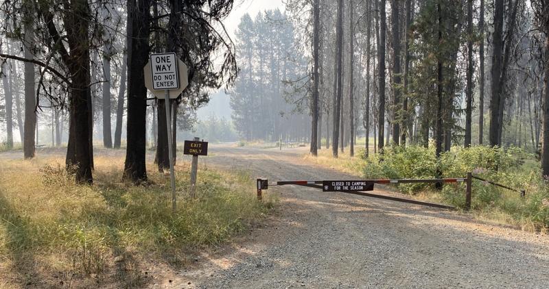 A closed gate at the Horsethief Reservoir campground with smoke in the background. 