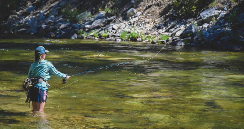woman fly fishing in summer along mountain river
