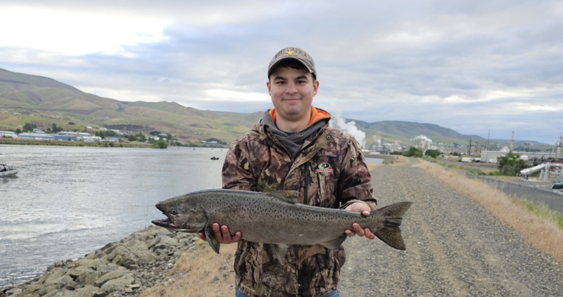 An angler stands along the Clearwater River with a Chinook salmon