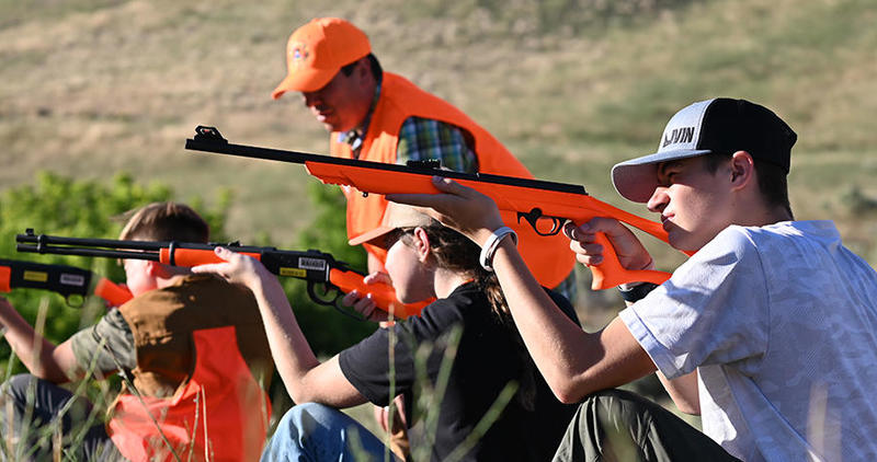 A hunter education instructor oversees students taking part in a field exercise with inert firearms.