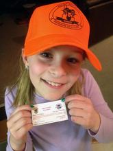 girl with her card after graduating from hunter education wearing a hunter orange cap small photo