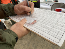 A Fish and Game staff member enters information on a CWD sample bag while holding a clipboard.