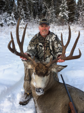 man with his big mule deer buck and rifle in snow vertical shot November 2016