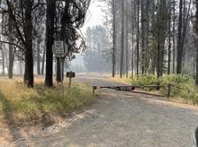 A closed gate at the Horsethief Reservoir campground with smoke in the background. 