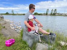 Father and daughter sitting on a rock fishing at Ryder Park next to a pink tackle box.