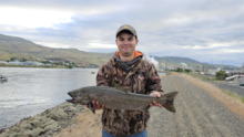 An angler stands along the Clearwater River with a Chinook salmon
