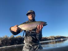 Man holds a large rainbow trout with a blue sky in the background