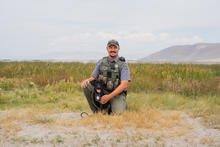 a black dog sits with its male owner/handler in a light green field