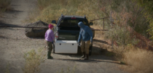 Two anglers carry a cooler to a pickup truck