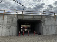 Gray concrete wildlife underpass under construction with a crane and cloudy sky in the background