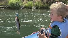 Kid on a raft smiling at a fish that was just caught.