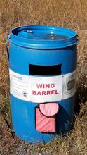  A blue barrel sits in a field of grass with the words "wing barrel" across it. 