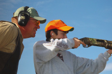 an instructor watches as a boy fires a rifle at a youth pheasant hunt November 2004